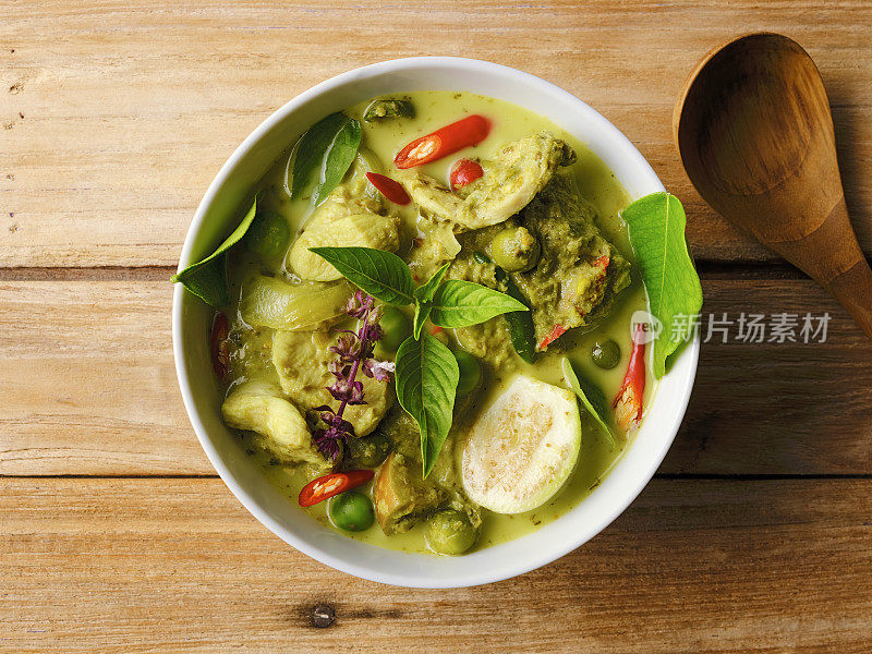 著名的国际知名的泰国绿色椰子咖喱'Gaeng Keow Wan Gai'，鸡肉，在一个碗，在一个旧的破旧的木制背景和一个木制的服务勺旁边的碗。